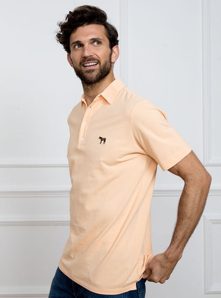 Man wearing peach coloured polo shirt in 100% cotton with Newmarket 875 horse logo embroidered on the front.
